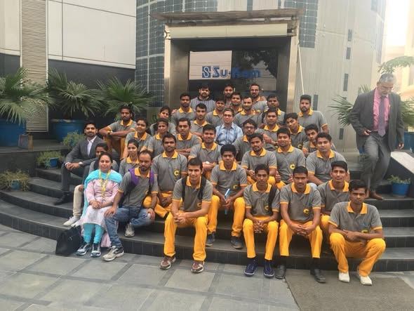 Su-Kam staff in company uniform on the steps of a Su-Kam building with solar-clad walls