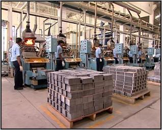 Battery manufacturing line with workers at process machines and stacked plates on pallets