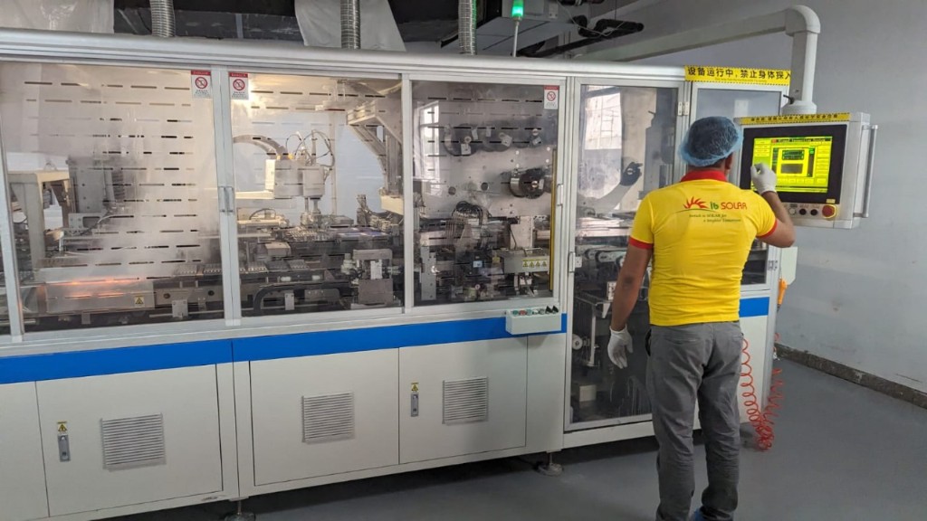Worker at Ib SOLAR operating an automated assembly machine with Chinese-language interface