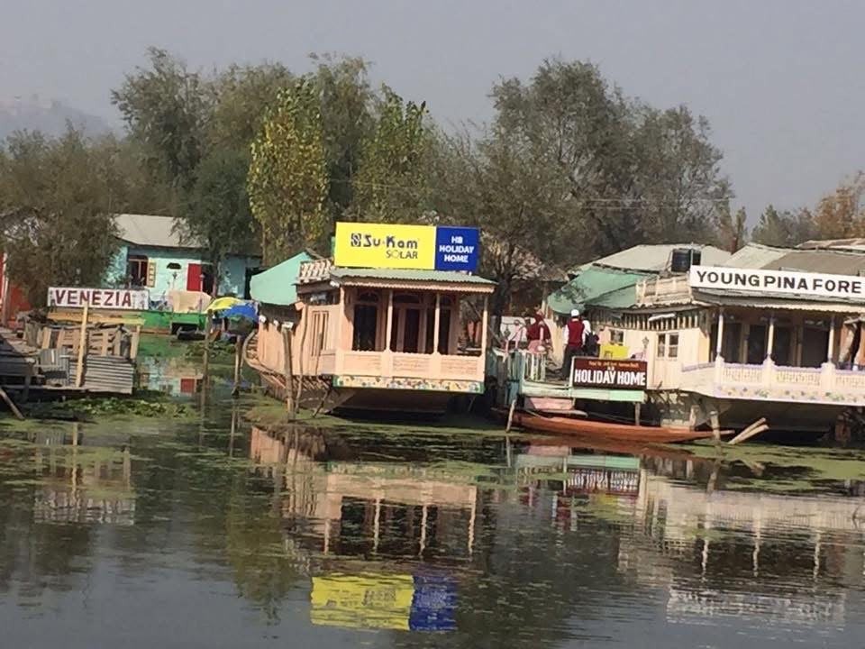 Houseboat on Dal Lake with yellow Su-Kam Solar rooftop sign and Holiday Home board