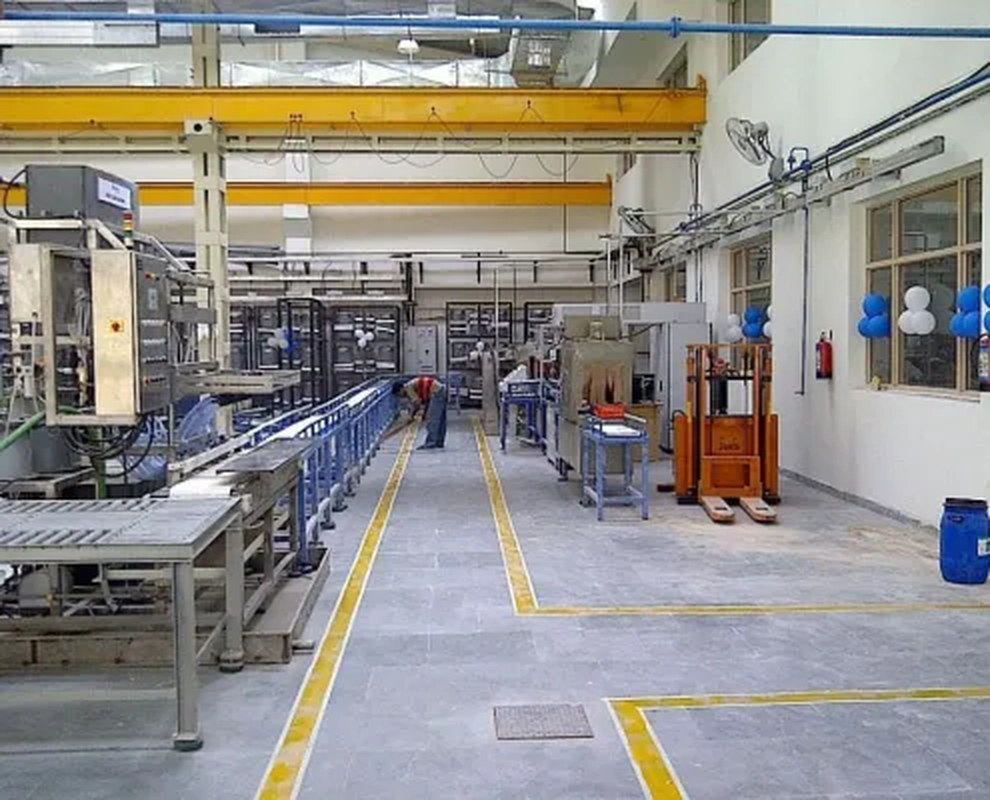 Su-Kam production aisle with blue assembly line, overhead crane, and technician on the floor
